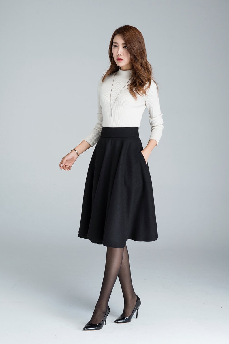 Peut inclure: Une jupe midi noire &agrave; taille haute avec une silhouette &eacute;vas&eacute;e. La jupe a un design simple avec deux poches sur le devant.