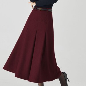 May include: A burgundy midi skirt with a high waist and a flared silhouette. The skirt is paired with a black long-sleeve top and a black belt. Black high heels complete the outfit.