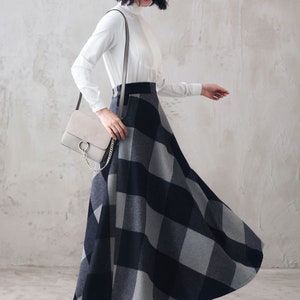May include: A woman wearing a white long-sleeved blouse with a black and gray plaid skirt. She is carrying a gray shoulder bag with a gold chain.
