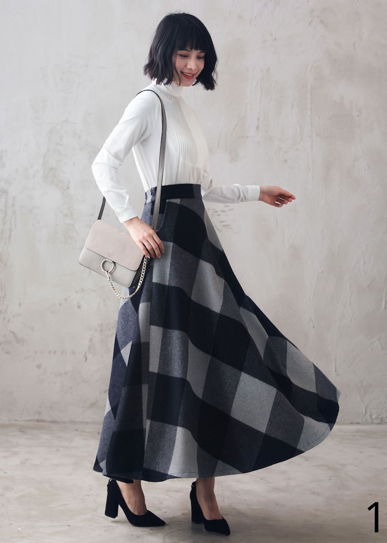 May include: A woman wearing a white long-sleeved blouse with a black and gray plaid skirt. She is carrying a gray shoulder bag with a gold chain.