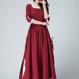 May include: A long, red maxi dress with white lace trim at the neckline and cuffs. The dress has a fitted bodice and a flowing skirt with a side slit.