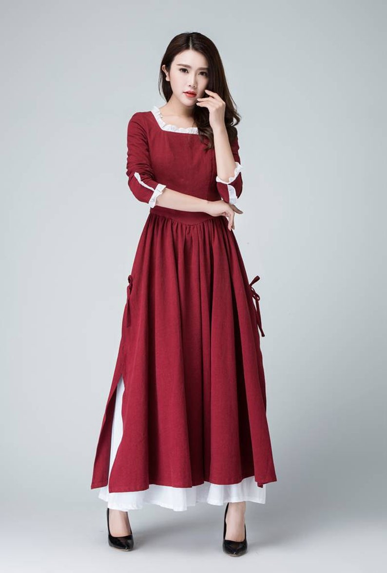May include: A long, red maxi dress with white lace trim at the neckline and cuffs. The dress has a fitted bodice and a flowing skirt with a side slit.