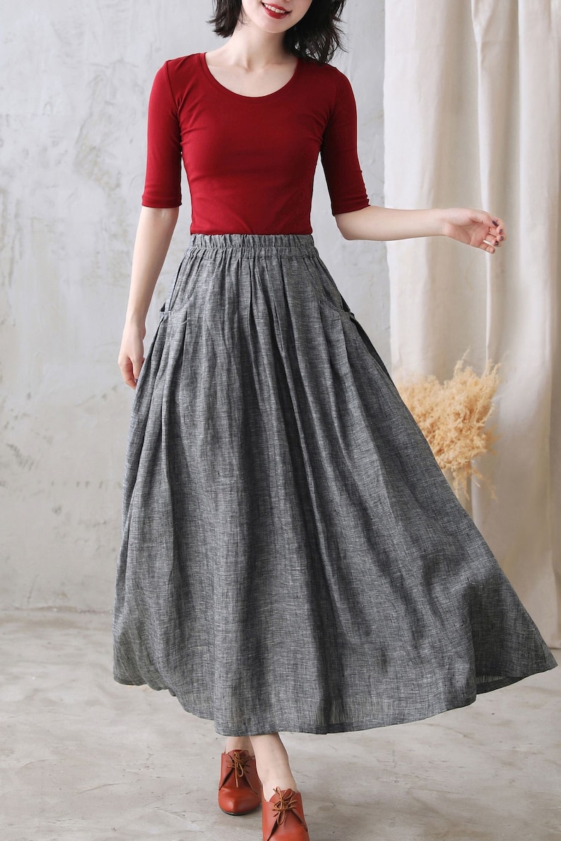 May include: A gray linen skirt with a wide, flowing silhouette and a high waist. The skirt has a relaxed fit and features two large pockets on the sides. The skirt is paired with a red fitted top.