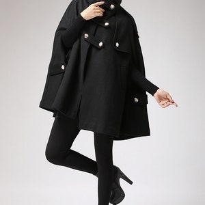 May include: A black hooded cape with a double-breasted button closure and pockets. The cape is made of a soft, warm fabric and has a relaxed fit.