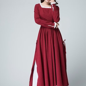 May include: A long, red dress with white lace trim at the neckline and cuffs. The dress has a fitted bodice and a full skirt. The model is wearing black heels.