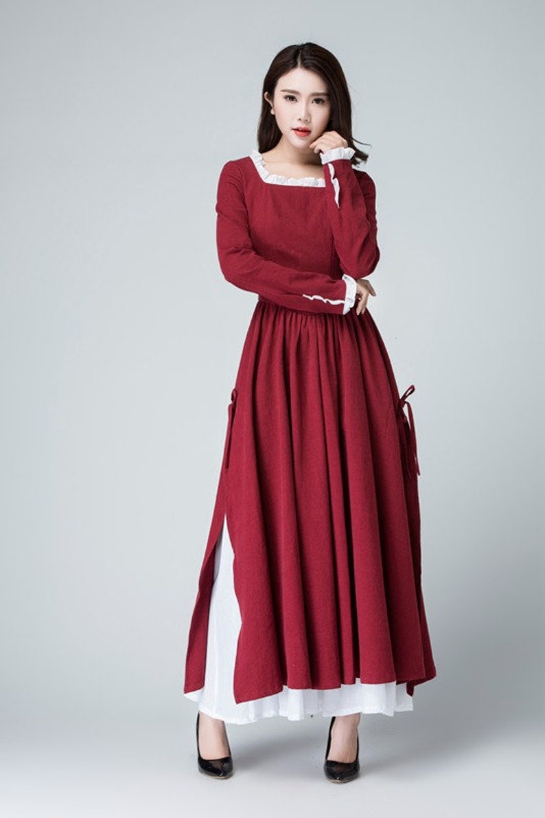 May include: A long, red dress with white lace trim at the neckline and cuffs. The dress has a fitted bodice and a full skirt. The model is wearing black heels.