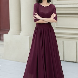 May include: A burgundy maxi dress with a sheer bodice and a gathered skirt. The dress has a round neckline and three-quarter sleeves.