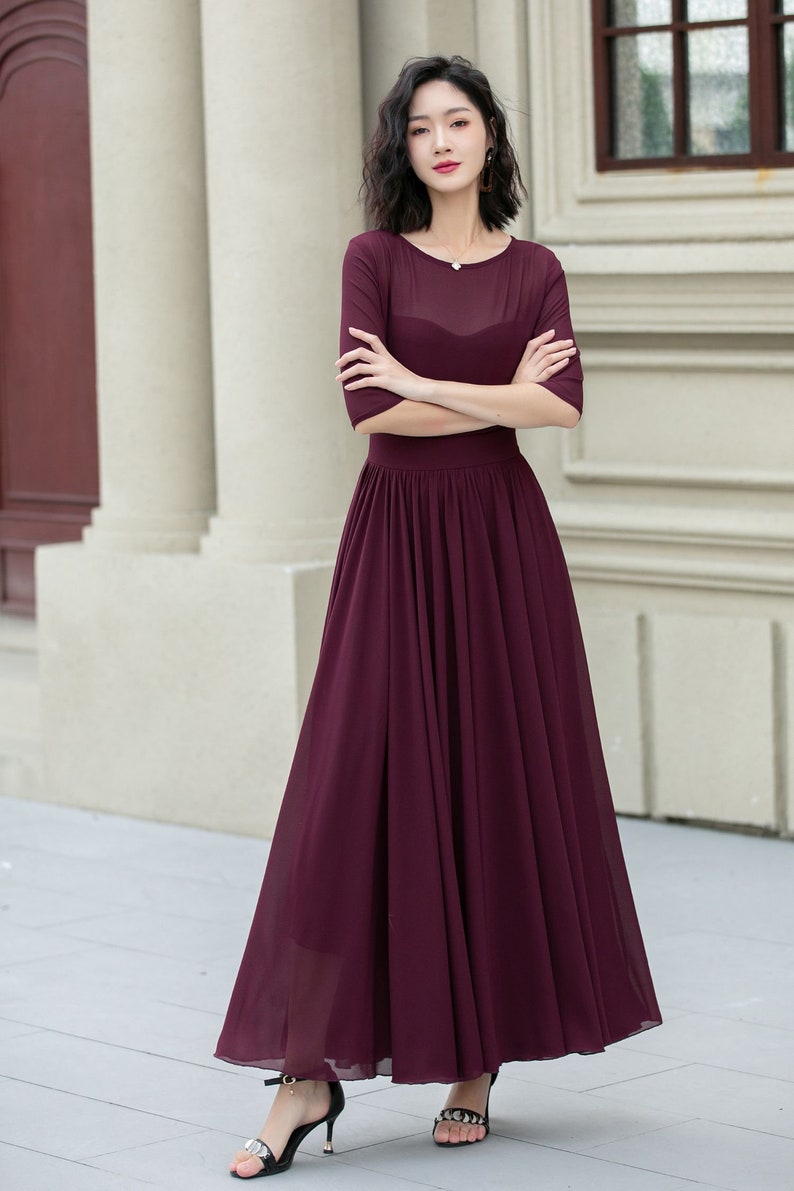 May include: A burgundy maxi dress with a sheer bodice and a gathered skirt. The dress has a round neckline and three-quarter sleeves.