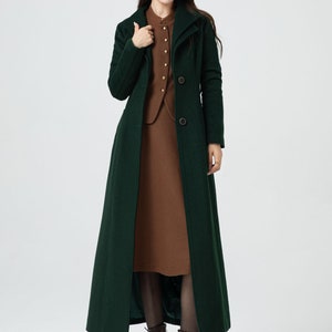 May include: A long, dark green coat with a high collar and button closure. The coat is worn over a brown dress and brown boots.