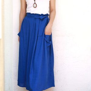 May include: A woman's outfit featuring a white tank top and a long, vibrant blue skirt. The skirt has a wrap-around design with a tie at the waist and pockets. The image is labeled "5-blue".