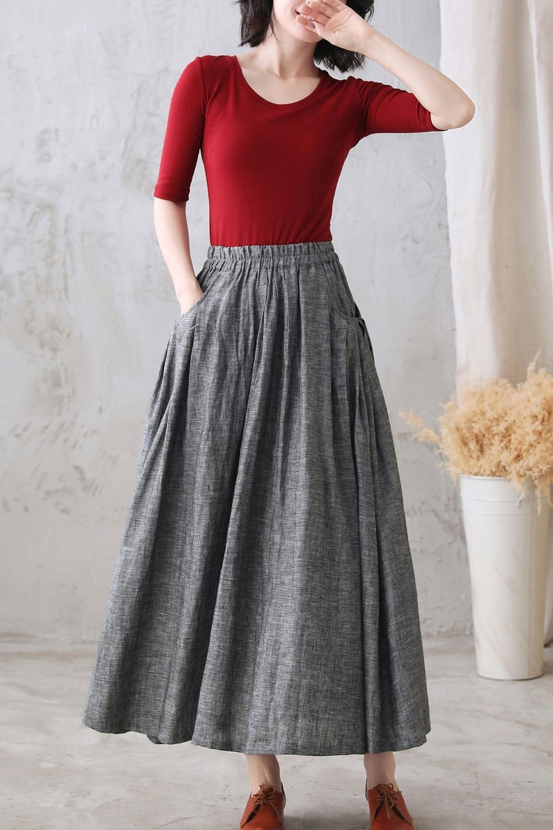May include: A gray linen skirt with a wide waistband and two large pockets. The skirt is pleated and falls to the ankles.