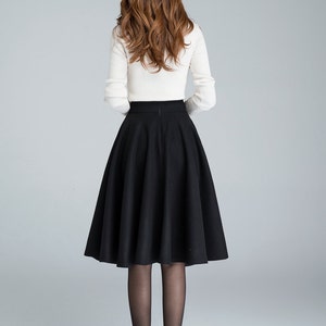 Peut inclure: Une jupe midi noire &agrave; taille haute et &agrave; silhouette &eacute;vas&eacute;e. La jupe est faite d'un tissu &eacute;pais et textur&eacute; et arrive juste en dessous du genou.