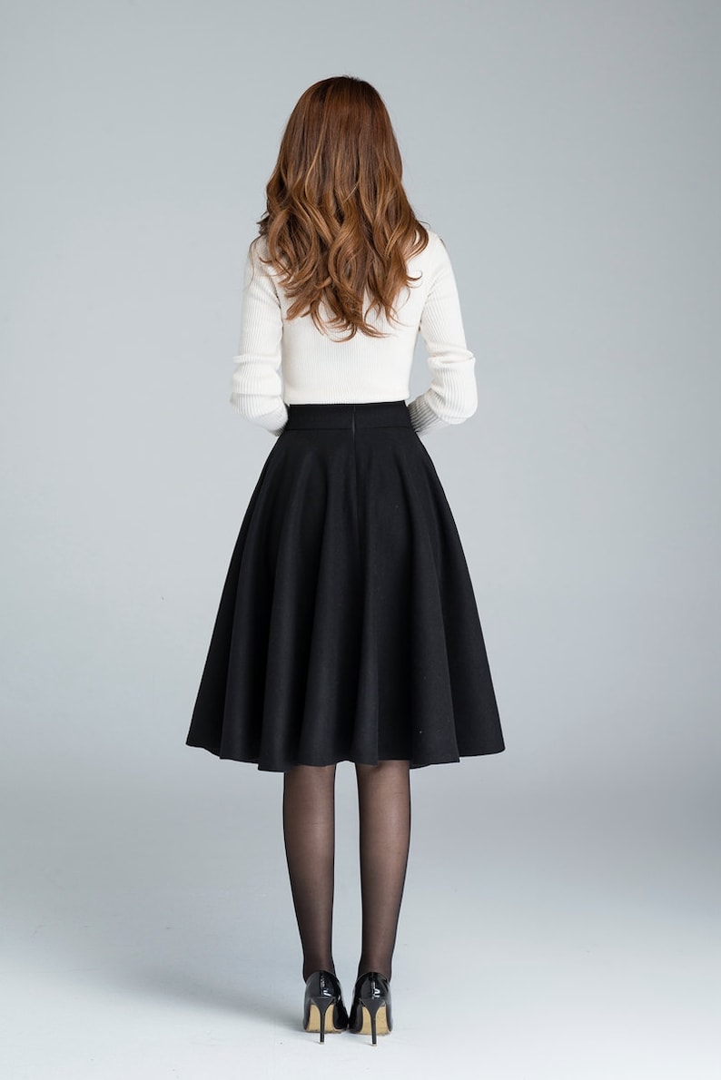 Peut inclure: Une jupe midi noire &agrave; taille haute et &agrave; silhouette &eacute;vas&eacute;e. La jupe est faite d'un tissu &eacute;pais et textur&eacute; et arrive juste en dessous du genou.