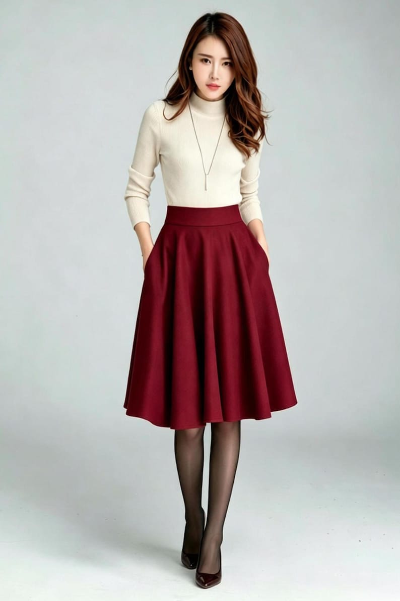May include: A cream-colored long-sleeve mock neck sweater paired with a high-waisted, knee-length, deep burgundy A-line skirt featuring side pockets. The outfit is completed with sheer black tights and dark-colored closed-toe pumps.