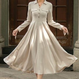 May include: A beige long-sleeved dress with a collared neckline, button closure, and a flared skirt.