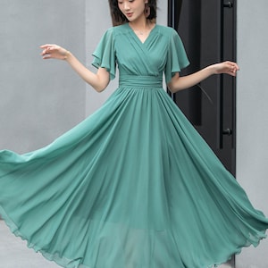 May include: A teal maxi dress with a V-neckline, short flutter sleeves, and a fitted waist. The dress has a flowing skirt and is made of a lightweight fabric.