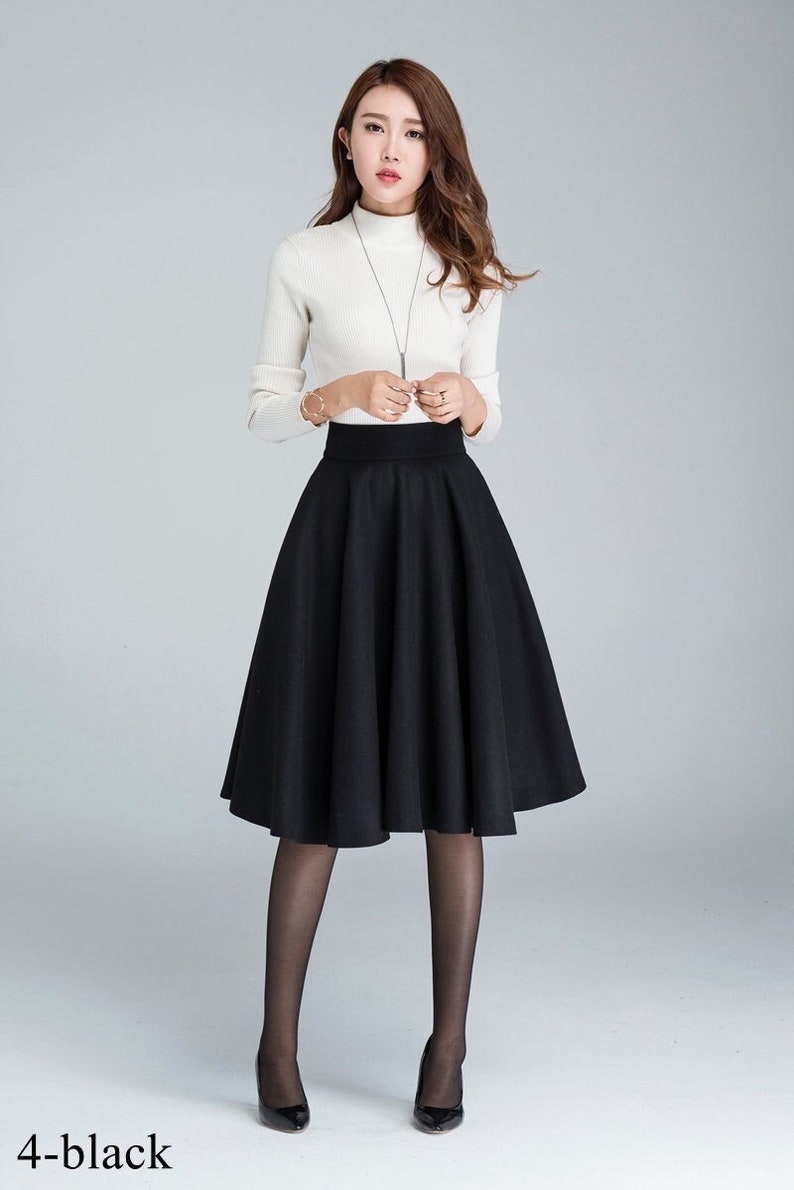 Peut inclure: Une jupe noire &agrave; taille haute avec une silhouette &eacute;vas&eacute;e. La jupe est mi-longue et faite d'un tissu lisse.
