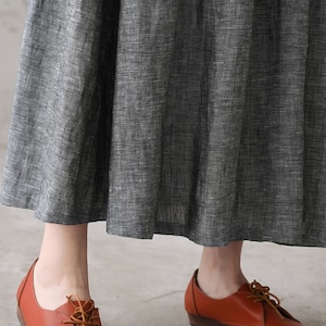 May include: A pair of brown leather lace-up shoes with a low heel. The shoes are worn by a person wearing a gray skirt.