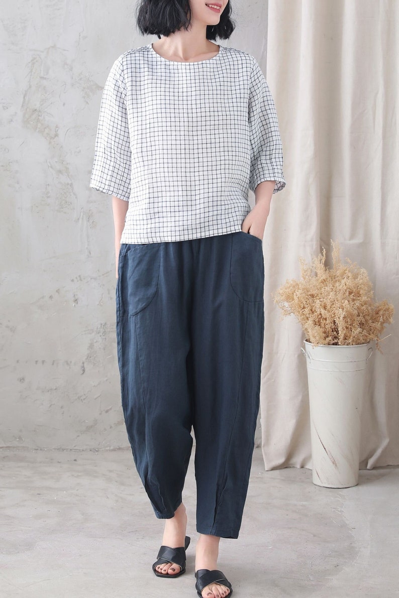 Op de afbeelding: Een wit en zwart geruit linnen top met een ontspannen pasvorm en 3/4 mouwen gecombineerd met een donkerblauwe linnen broek met zakken. De broek heeft een wijde pijp en een ontspannen pasvorm.