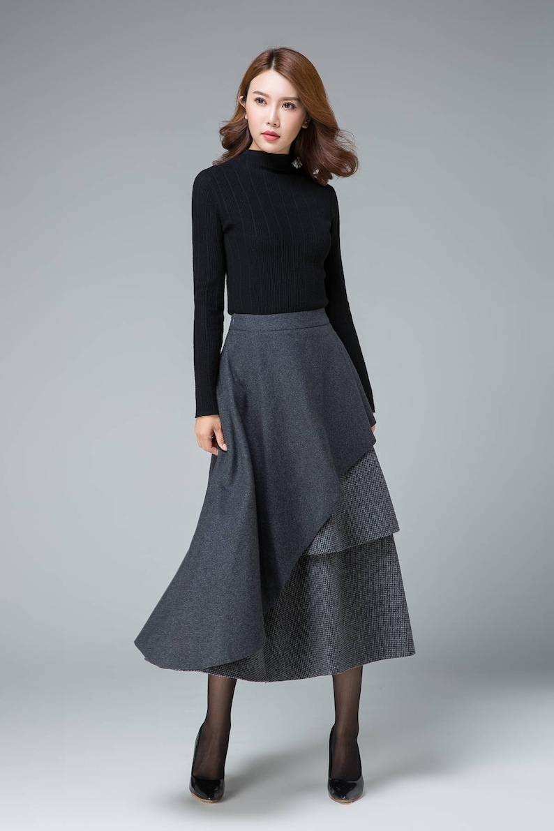 May include: A woman wearing a black turtleneck sweater and a gray layered skirt. The skirt has a longer, flowing layer on top of a shorter, patterned layer.