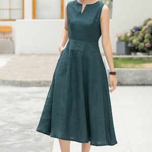 Peut inclure: Une femme portant une robe midi sans manches de couleur vert fonc&eacute; avec un d&eacute;collet&eacute; en V. Elle est debout sur un trottoir et porte des sandales brunes.