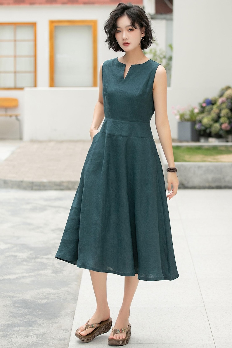 Peut inclure: Une femme portant une robe midi sans manches de couleur vert fonc&eacute; avec un d&eacute;collet&eacute; en V. Elle est debout sur un trottoir et porte des sandales brunes.