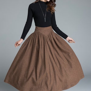 May include: A brown wool midi skirt with a high waist and pleats. The skirt is fitted at the waist and flares out to a full, A-line shape.