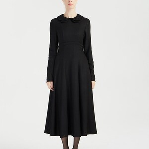 Puede incluir: Un vestido negro de manga larga con cuello de Peter Pan y falda acampanada.