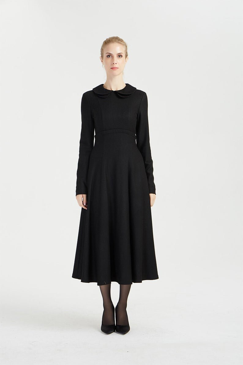 Puede incluir: Un vestido negro de manga larga con cuello de Peter Pan y falda acampanada.