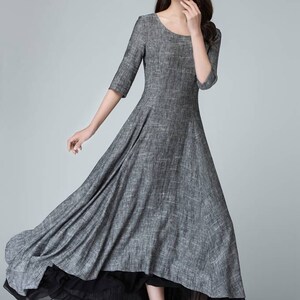 K&ouml;nnte beinhalten: Ein graues Leinen-Maxikleid mit einem schwarzen Chiffon-Unterrock. Das Kleid hat einen runden Ausschnitt und 3/4 &Auml;rmel. Das Model tr&auml;gt schwarze Abs&auml;tze.