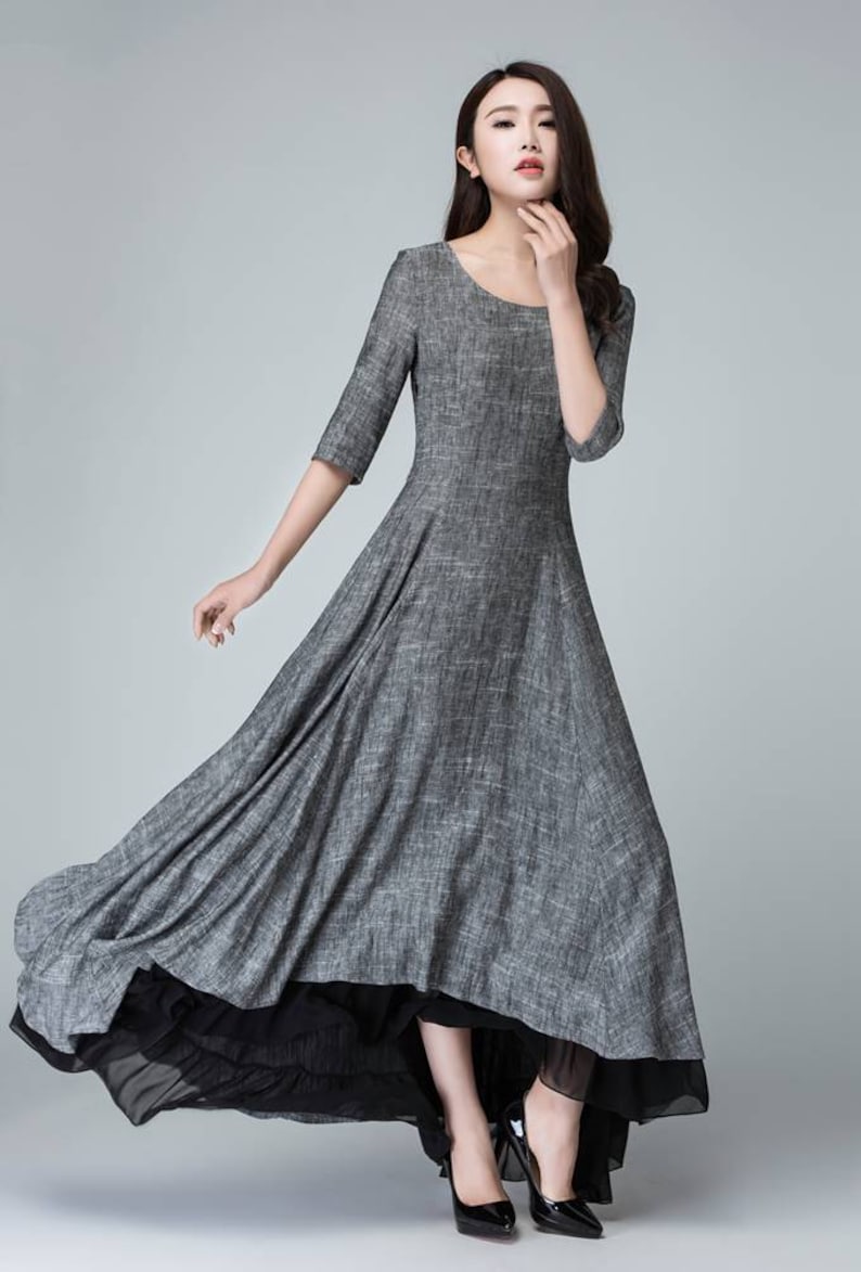 K&ouml;nnte beinhalten: Ein graues Leinen-Maxikleid mit einem schwarzen Chiffon-Unterrock. Das Kleid hat einen runden Ausschnitt und 3/4 &Auml;rmel. Das Model tr&auml;gt schwarze Abs&auml;tze.