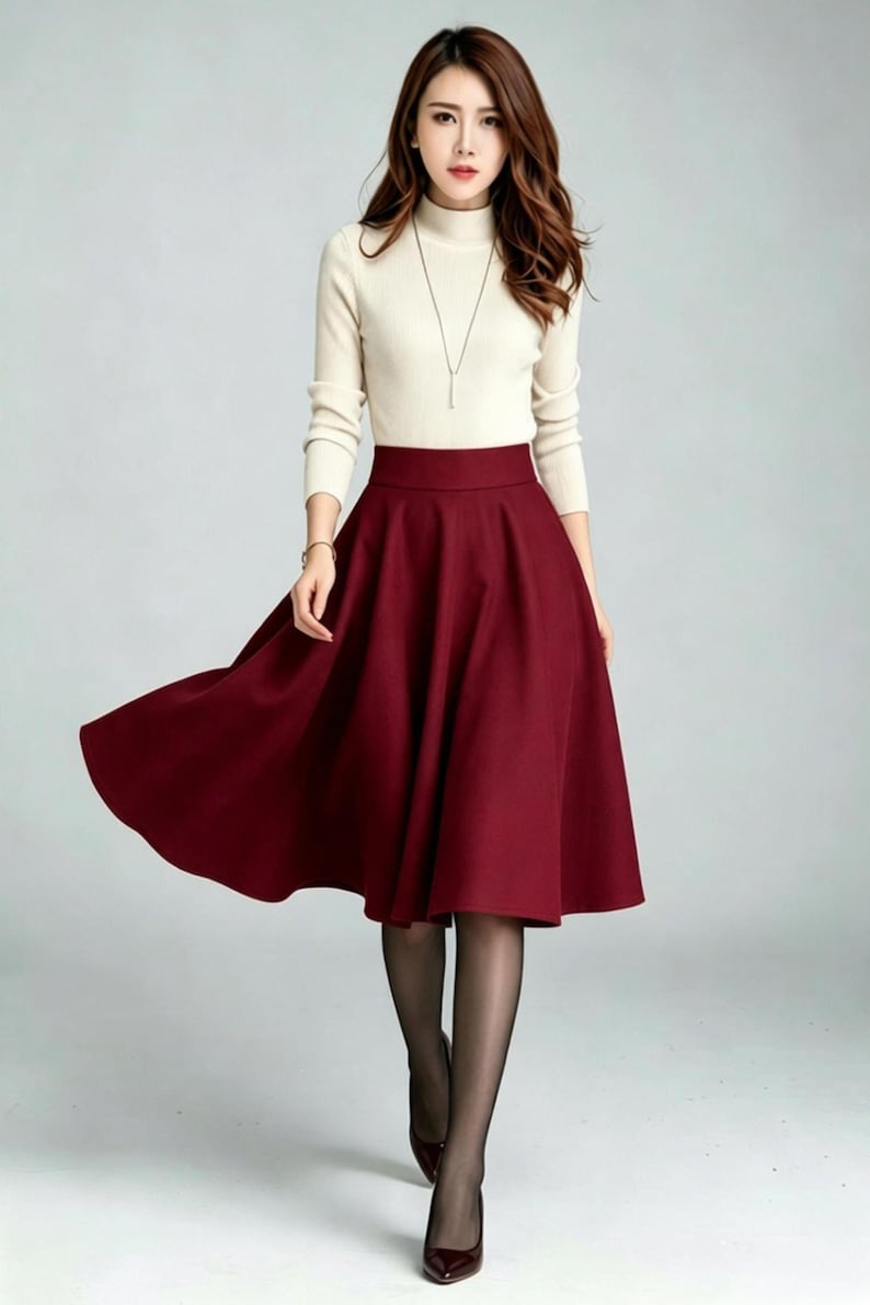 May include: A cream-colored long-sleeve mock neck sweater paired with a solid deep burgundy midi-length skirt. The skirt features a high-waisted design with a flared, A-line silhouette that falls below the knees, complemented by sheer black tights.