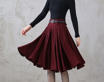 May include: A burgundy midi skirt with a black belt and a silver buckle. The skirt is pleated and has a flared silhouette.