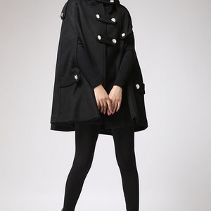May include: A black hooded cape with silver buttons and pockets. The cape is made of a soft, warm fabric and has a relaxed fit.