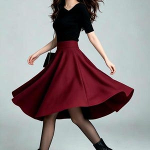 May include: A black short-sleeved top with a V-neckline paired with a high-waisted, flared midi skirt in a deep burgundy red color. The outfit is completed with sheer black tights and black pointed-toe ankle boots with a high stiletto heel.