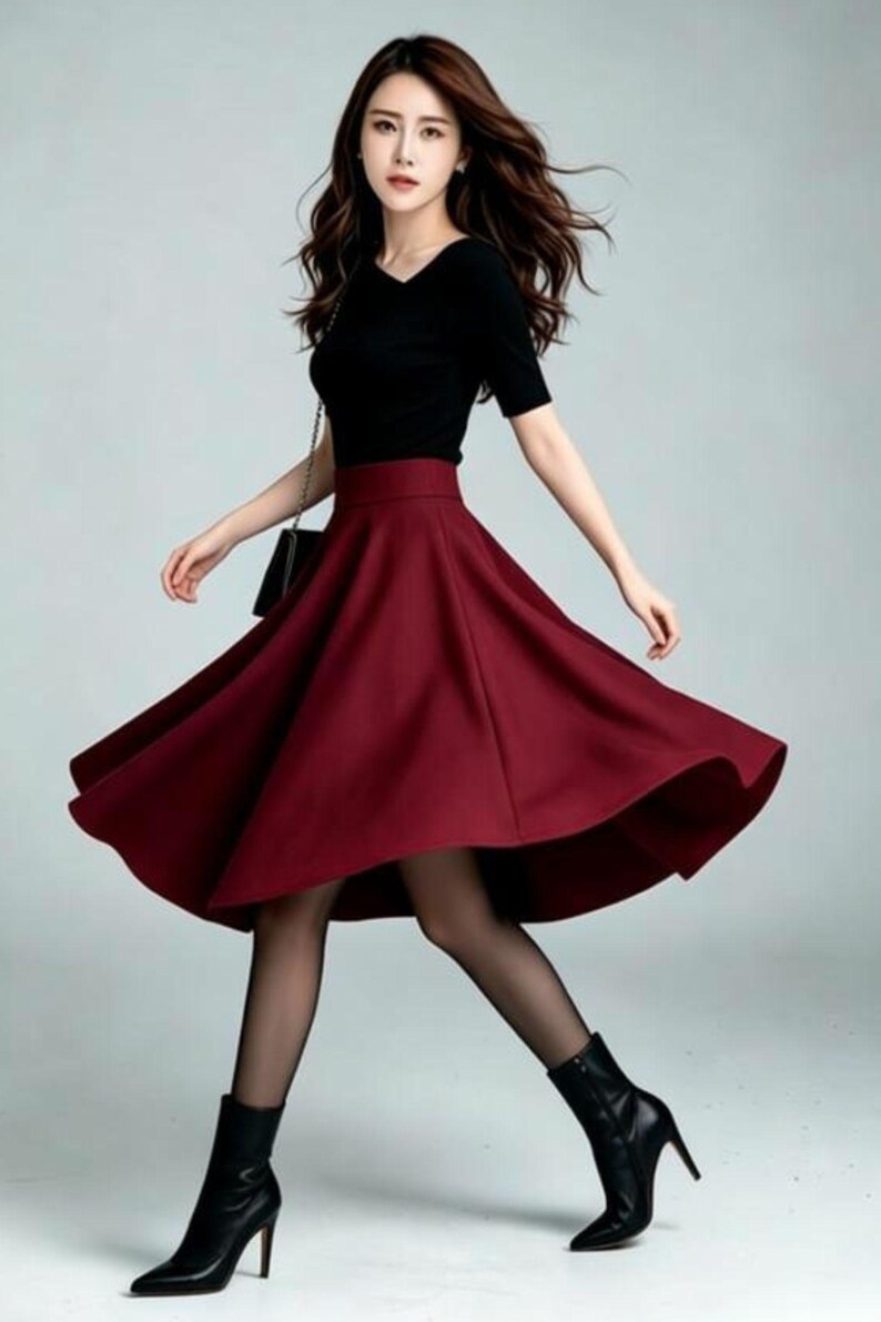 May include: A black short-sleeved top with a V-neckline paired with a high-waisted, flared midi skirt in a deep burgundy red color. The outfit is completed with sheer black tights and black pointed-toe ankle boots with a high stiletto heel.