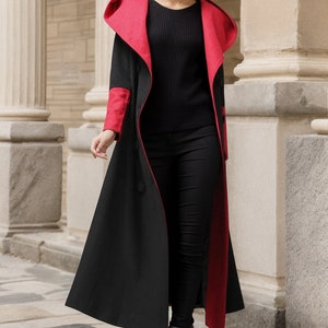 May include: A long black coat with a red hood and red trim. The coat has a double-breasted closure and a long, flowing silhouette.