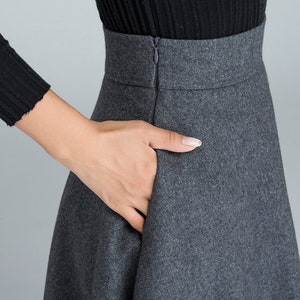 K&ouml;nnte beinhalten: Ein grauer Wollrock mit Rei&szlig;verschluss hinten. Der Rock hat eine hohe Taille und eine ausgestellte Silhouette.
