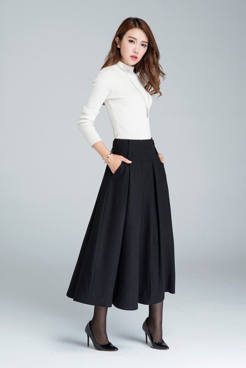 May include: A black high-waisted skirt with pleats and a flared hem. The skirt is worn with a white turtleneck sweater and black heels.