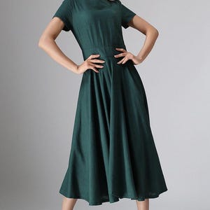 Puede incluir: Un vestido midi de color verde oscuro con escote redondo, mangas cortas y una cintura entallada que da paso a una falda amplia y plisada. La prenda est&aacute; confeccionada en un tejido de color s&oacute;lido y llega por debajo de las rodillas.