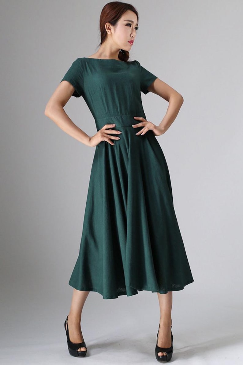 Puede incluir: Un vestido midi de color verde oscuro con escote redondo, mangas cortas y una cintura entallada que da paso a una falda amplia y plisada. La prenda est&aacute; confeccionada en un tejido de color s&oacute;lido y llega por debajo de las rodillas.