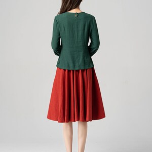 May include: A woman wearing a green long-sleeved blouse and a red midi skirt. She is wearing black high heels.