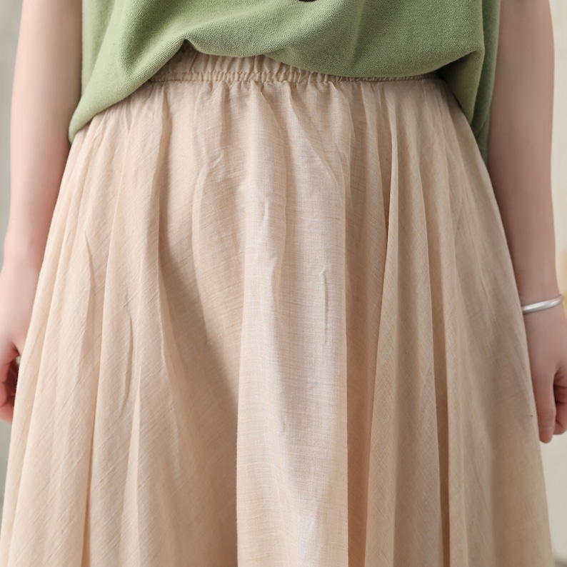 May include: A beige skirt with an elastic waistband and a flowing, pleated design. The skirt is paired with a green top. The fabric appears to be lightweight and suitable for warm weather.