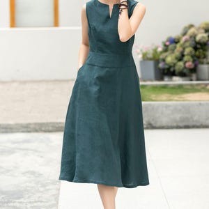 Peut inclure: Une robe en lin sans manches, de couleur vert fonc&eacute;, avec un col en V et une jupe l&eacute;g&egrave;rement &eacute;vas&eacute;e. La robe a des poches sur les c&ocirc;t&eacute;s et est port&eacute;e avec des sandales brunes.