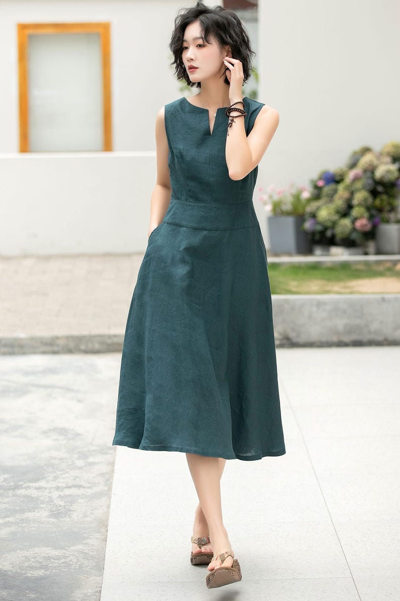 Peut inclure: Une robe en lin sans manches, de couleur vert fonc&eacute;, avec un col en V et une jupe l&eacute;g&egrave;rement &eacute;vas&eacute;e. La robe a des poches sur les c&ocirc;t&eacute;s et est port&eacute;e avec des sandales brunes.