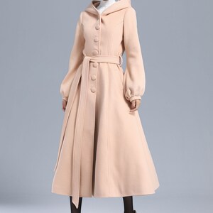 May include: A long, light pink coat with a hood, a belt, and button closures. The coat has a flared skirt and long sleeves.