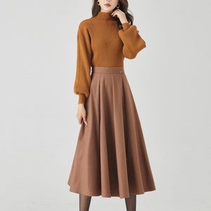 May include: A brown midi skirt with a high waist and a flared silhouette. The skirt is paired with a brown turtleneck sweater with long sleeves and a ribbed texture.