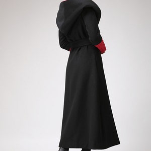 May include: A long black hooded coat with a red trim around the hood and cuffs. The coat has a belt and a flowing skirt.