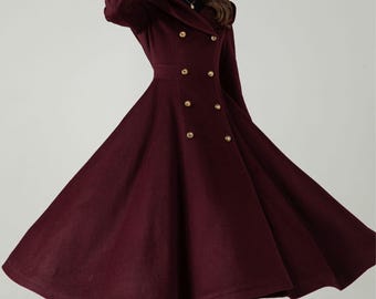 May include: A burgundy double-breasted coat with gold buttons and a flared skirt. The long coat features a fitted waist and a wide, flowing skirt. The sleeves have gold buttons at the cuffs. A black hat completes the look.