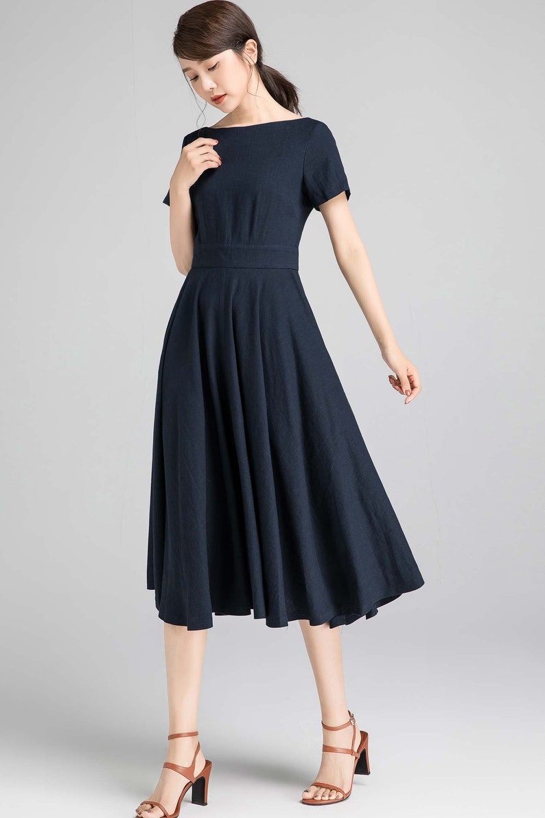 May include: A navy blue midi dress with a boat neck and short sleeves. The dress has a fitted bodice and a flowing skirt.